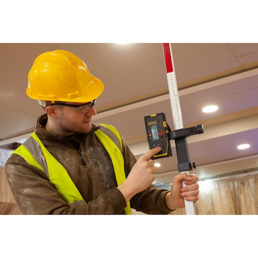 STANLEY FMHT77652-0 récepteur laser tenu par un ouvrier, fixé à une tige de mesure.