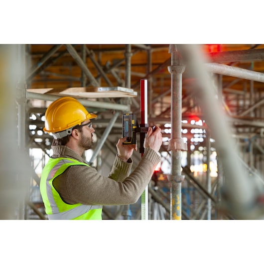 Niveau laser STANLEY FMHT77652-0 utilisé sur chantier par un ouvrier équipé de sécurité.