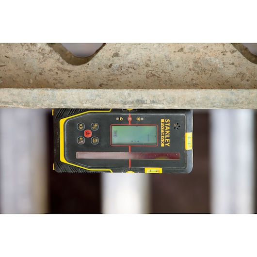 Détecteur laser STANLEY FMHT77652-0 avec écran, vue de dessus, boîtier noir et jaune, contexte chantier.