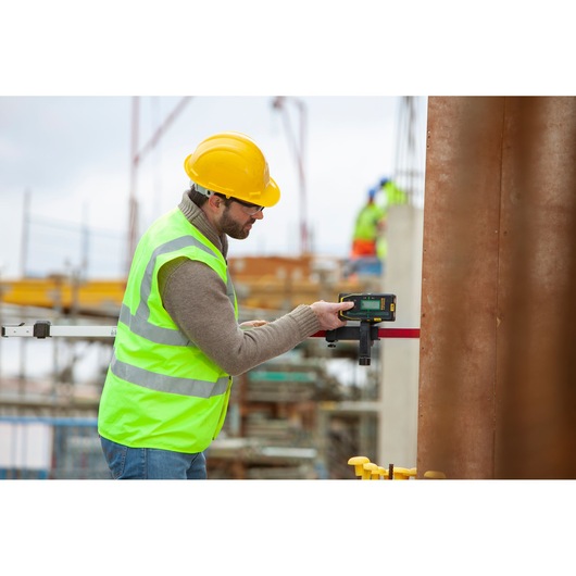 STANLEY FMHT77653-0 laser detector vastgehouden door werknemer met veiligheidshes en helm op bouwplaats.