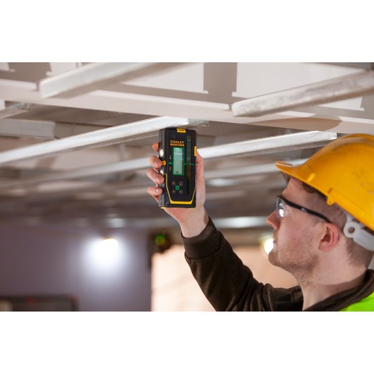 STANLEY FMHT77653-0 laserwaterpas vastgehouden door werknemer met gele helm bij meten van metalen plafondframe.