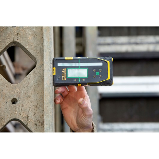 STANLEY FMHT77653-0 laser detector door hand tegen beton gehouden, bouwplaats achtergrond.