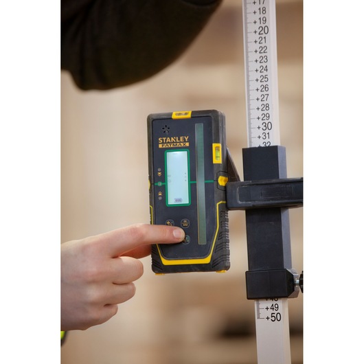 STANLEY FMHT77653-0 laser detector vastgehouden door hand, bevestigd aan meetlat, close-up fotografie.