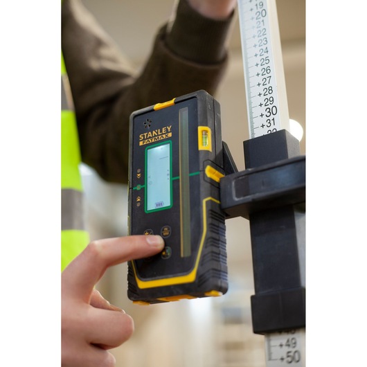 STANLEY FMHT77653-0 laserdetector vastgehouden door iemand die een knop indrukt, naast een meetlat.