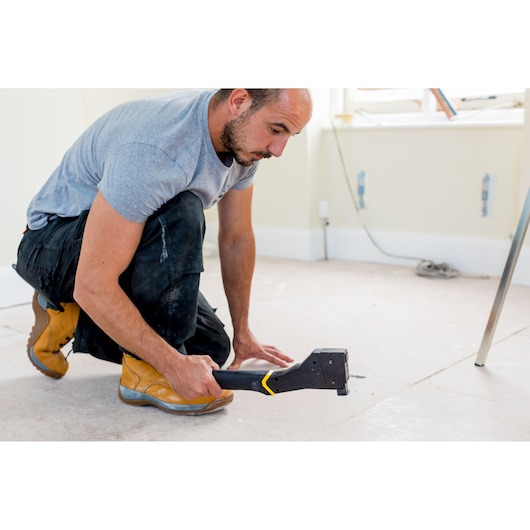Agrafeuse STANLEY FMHT81394-9 utilisée par un ouvrier sur chantier, photographie angle latéral.