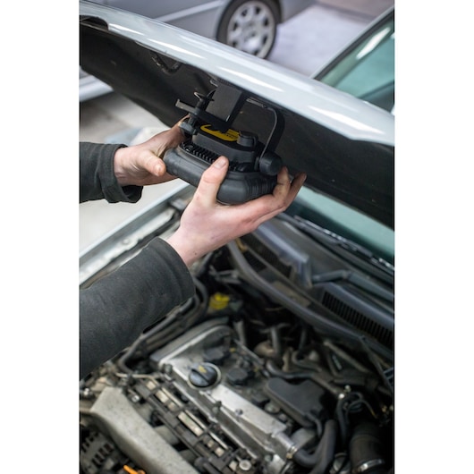 Photo d'une personne installant une lampe de travail STANLEY FMHT81507-1 sous le capot d'une voiture, axée sur l'installation.