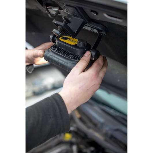 Lampe de travail STANLEY FMHT81507-1 fixée sous le capot d’une voiture, mains ajustant la lampe noire et jaune.