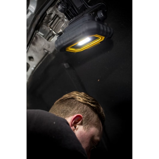 Lampe de travail STANLEY FMHT81507-1 fixée sous le capot, éclairant la zone moteur pendant la réparation.