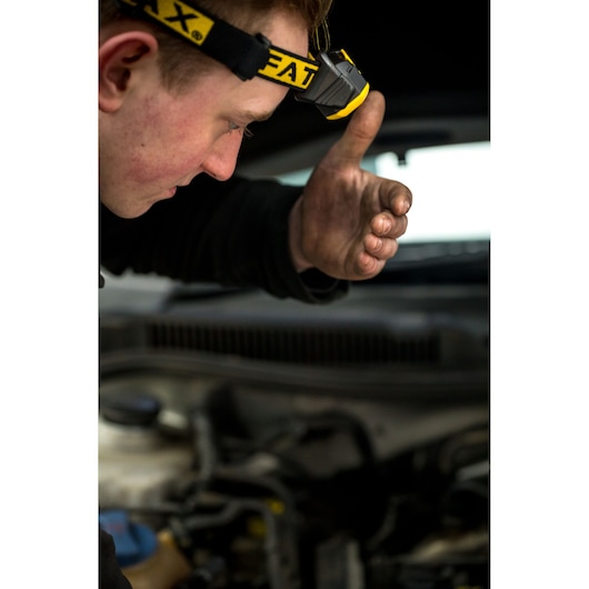 Foto van STANLEY FMHT81509-0 hoofdlamp gedragen door monteur met vuile hand bij de motor.