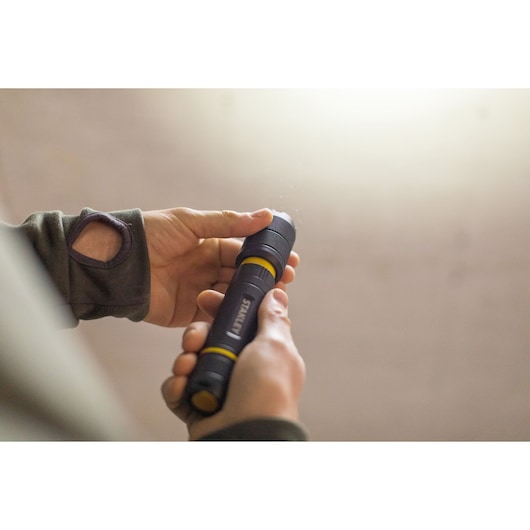 Foto van STANLEY FMHT81511-0 zwarte en gele zaklamp die in de hand wordt vastgehouden.