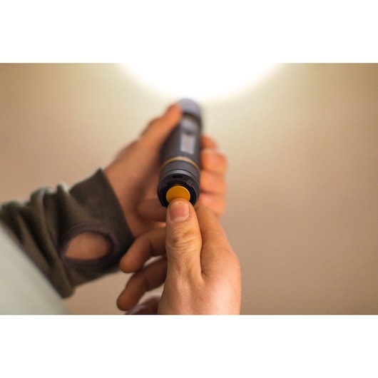 STANLEY FMHT81511-0 zaklamp in hand, gele knop ingedrukt, close-up fotografie.