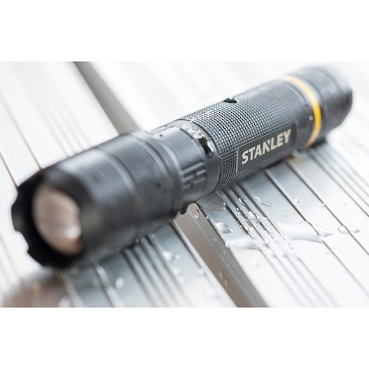 STANLEY FMHT81511-0 zwarte zaklamp met textuur grip en gele ring, close-up met waterdruppels.