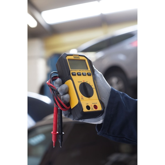 STANLEY FMHT82563-0 slimme digitale multimeter, geel en zwart, met meetpennen in een autogarage.