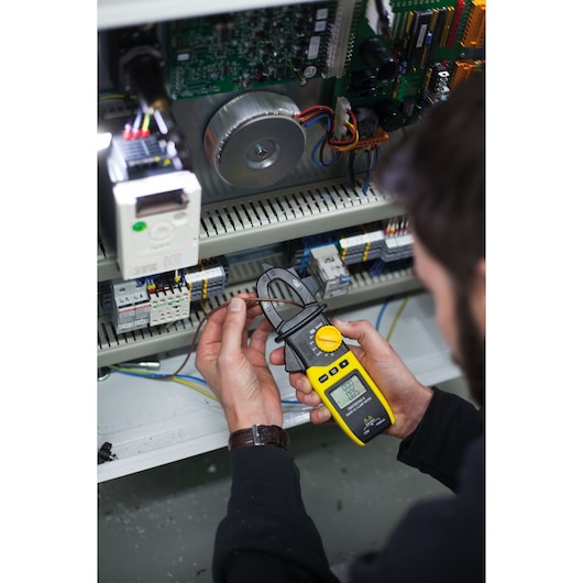Photo du multimètre à pince STANLEY FMHT82564-0 utilisé pour mesurer le courant électrique dans un panneau de contrôle ouvert.