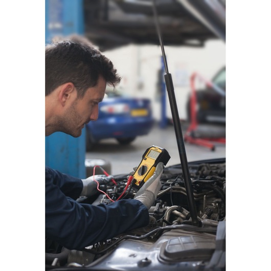 Foto van STANLEY FMHT82565-0 digitale multimeter in gebruik door monteur die een automotor test.