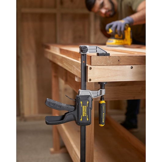 STANLEY FMHT83006-0 serre-joint à barre avec poignée jaune et noire sur établi en bois, photographie latérale.