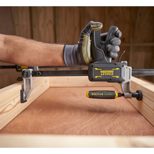Outil serre-joint STANLEY FMHT83006-0 tenu par une main gantée, installation de menuiserie, vue latérale.