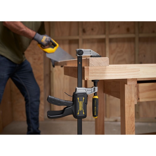 STANLEY FMHT83008-0 serre-joint fixant du bois sur un établi, personne sciant du bois dans un atelier.