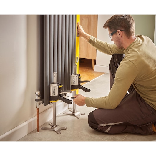 Foto van STANLEY FMHT83550-1 klemmen die een radiator vastzetten tijdens installatie, gebruikt door een persoon.