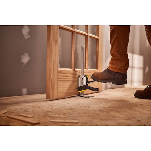STANLEY FMHT83550-1 deurbewerkingsklem in gebruik op houten deur, vakman bedient het gereedschap met de voet.