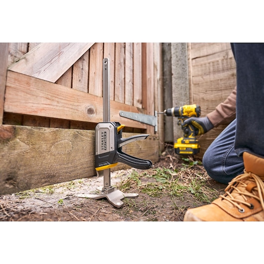 Foto van STANLEY FMHT83550-1 deurinstallatieklem die een houten poort buiten vasthoudt tijdens montage.