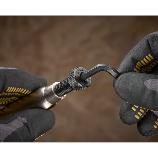 Mains gantées ajustent un outil métallique avec une clé hexagonale, fond marron flou.
