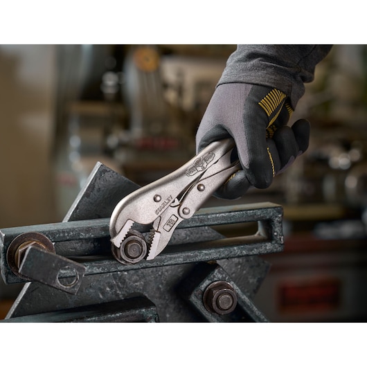 Main gantée utilise des pinces STANLEY pour saisir un boulon métallique dans un atelier.