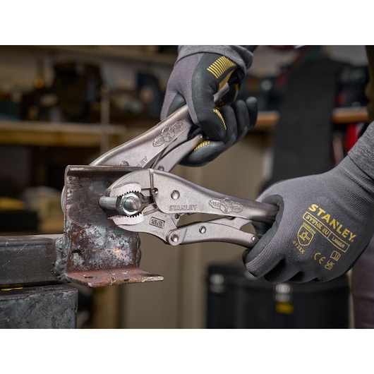 Pince étau Stanley tenue par des mains gantées, saisissant une pièce métallique en atelier.