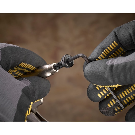 Mains gantées utilisent une clé Allen pour serrer un boulon sur un outil métallique.