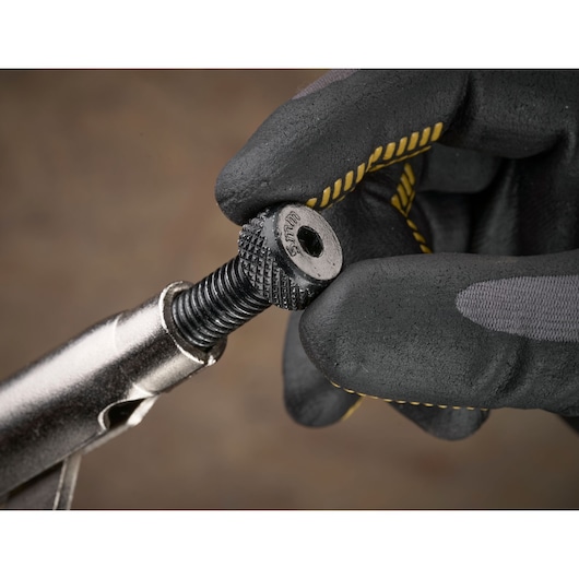 Main gantée ajustant une vis métallique STANLEY avec grip texturé sur un fond flou.