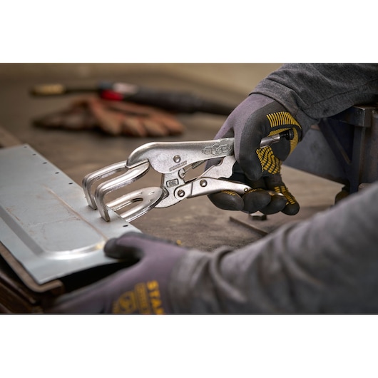 Une personne utilise une pince STANLEY pour maintenir une plaque métallique, portant des gants.