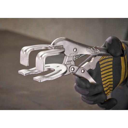 Une personne tient une pince étau STANLEY C-clamp, conçue pour le serrage et le soudage, avec un gant.