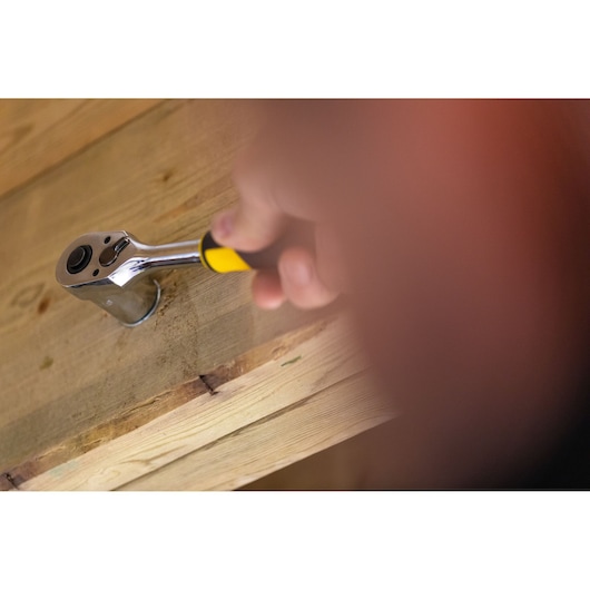 STANLEY FMMT82676-0 ratelsleutel met gele handgreep in gebruik op houten oppervlak.