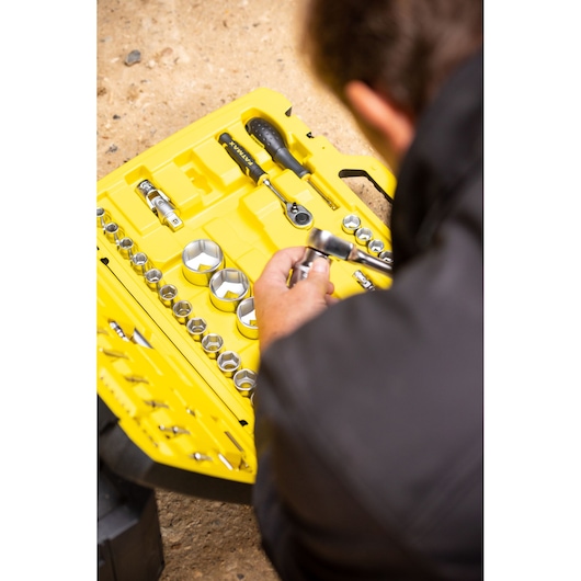 STANLEY FMMT82683-0 doppenset in gele koffer met diverse doppen en ratel, persoon houdt gereedschap vast.