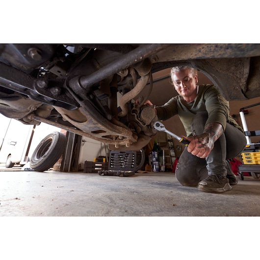 STANLEY FMMT82827-1 dopsleutel- en steeksleutelset in gebruik onder een auto in een garage, monteur werkt aan ophanging.