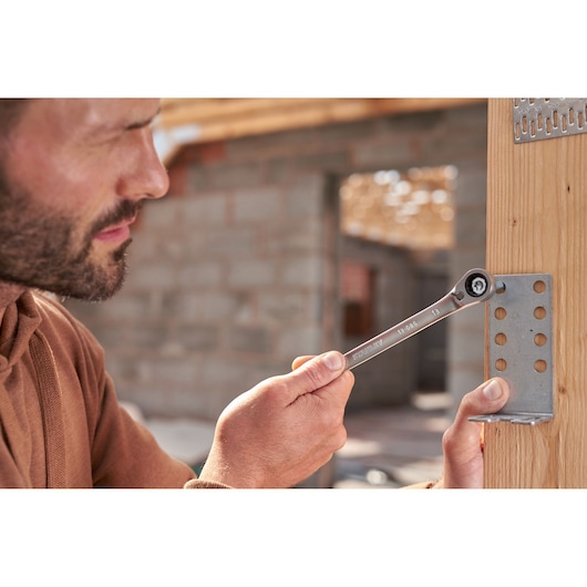 Clé à cliquet réversible STANLEY FMMT82848-0 utilisée pour serrer un boulon sur un support métallique fixé au bois.