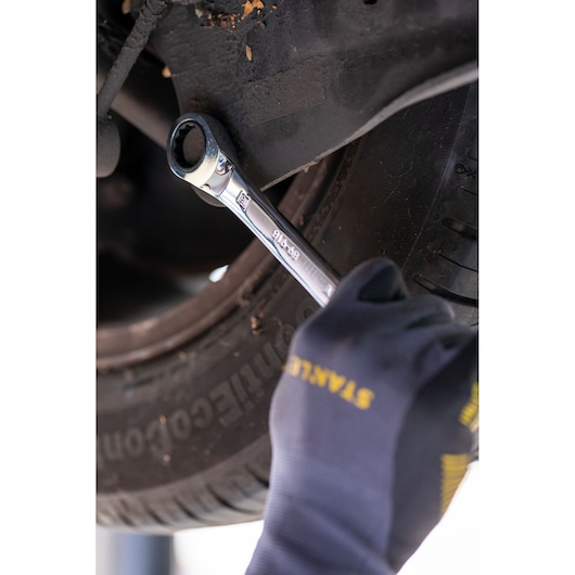 Foto van STANLEY FMMT82849-0 ratelringsleutel in gebruik op auto, hand met STANLEY handschoen.