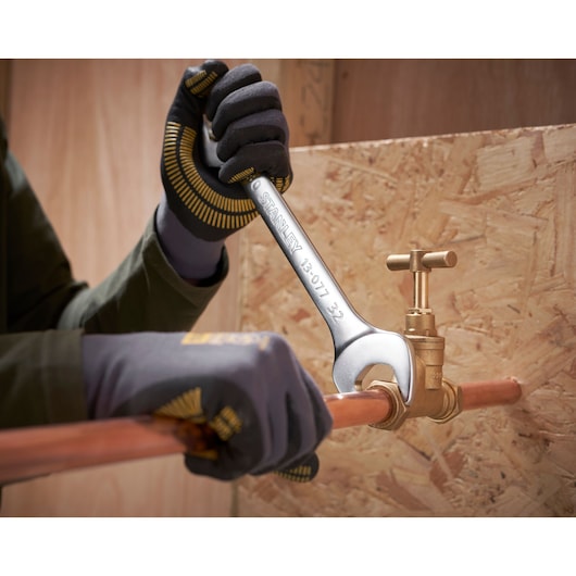 Foto van STANLEY FMMT82902-0 steeksleutel die een messing klep op koperen buis vastdraait, werknemer met handschoenen.