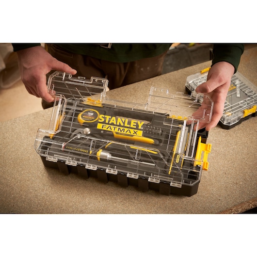 STANLEY FMMT98106-1 gereedschapsset met transparant deksel op werkbank, gele en zwarte gereedschappen.