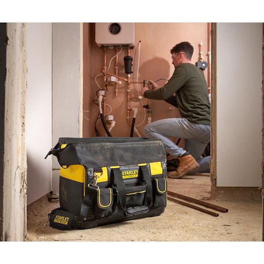 Sac à outils STANLEY FMST1-71180 noir et jaune avec poches extérieures, posé sur le sol d’un chantier.