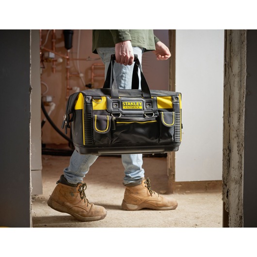 Sac à outils STANLEY FMST1-71180 noir et jaune, porté par une personne en bottes de travail, intérieur.