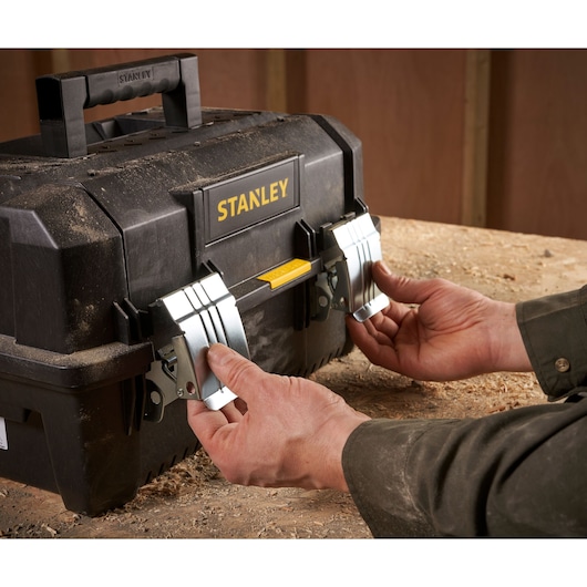 STANLEY FMST1-71219 boîte à outils noire avec loquets métalliques sur établi, mains ouvrant les serrures avant