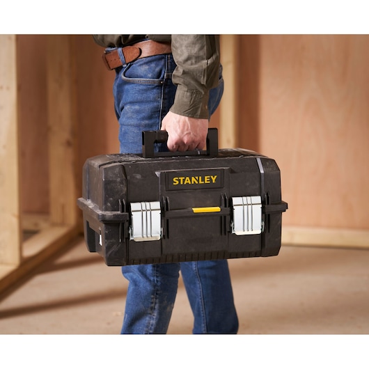 Boîte à outils Stanley FMST1-71219 avec fermetures métalliques et poignée, portée dans un atelier.