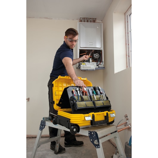 Photo de la mallette à outils STANLEY FMST1-72383 ouverte sur un escabeau, technicien travaillant sur une unité murale.
