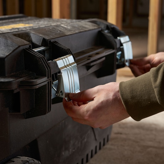 STANLEY FMST1-73601 boîte à outils avec loquets métalliques, gros plan des mains fermant les verrous avant.