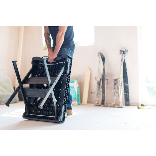Stanley FMST1-75672 werkbank opgevouwen, zwart kunststof frame, gedragen door een persoon.
