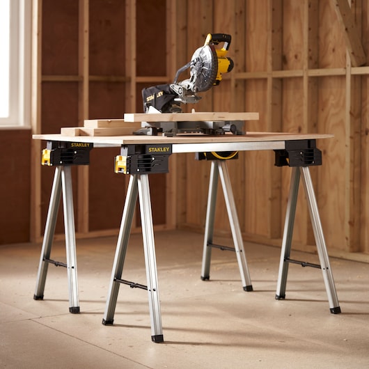 Foto van STANLEY FMST1-75763 werkstandaard met verstekzaag en houten planken in een werkplaats.