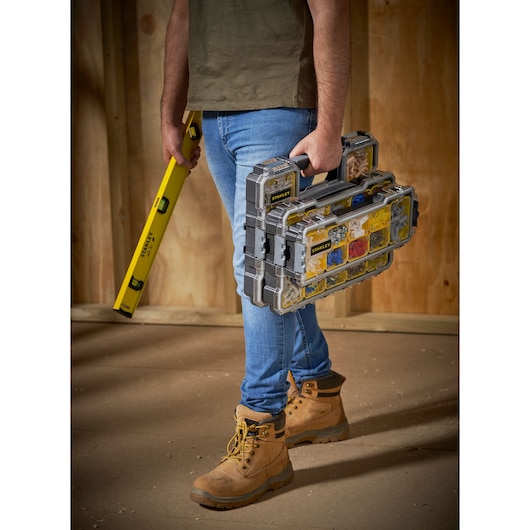 Photo de l’organisateur empilable STANLEY FMST1-75779 porté par un travailleur avec niveau, bottes et jeans.