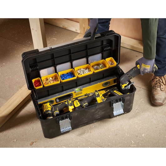 STANLEY FMST1-75791 gereedschapskist met gele compartimenten en elektrisch gereedschap, bovenaanzicht op werkplaatsvloer.
