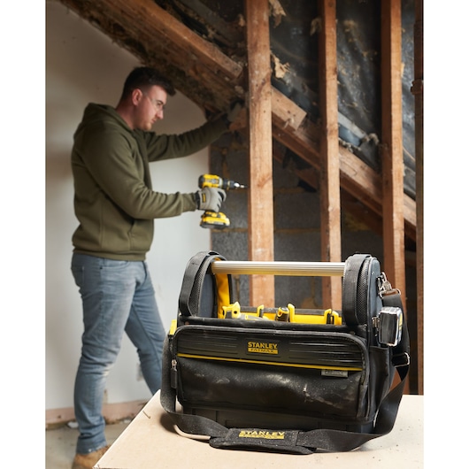 Sac à outils STANLEY FMST17626-1 avec accents jaunes sur table, personne travaillant en arrière-plan.